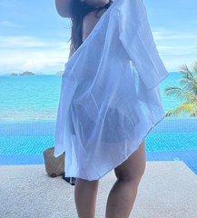 Woman in a white linen cover-up and sun hat by a pool with ocean view